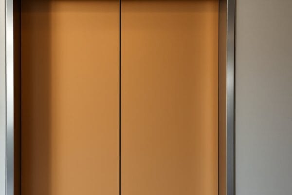 Closed elevator doors painted a matte ochre color inside a steel frame in a lobby