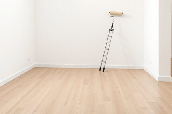 An empty white walled gallery room with a pale wood floor and a paint roller propped against the wall