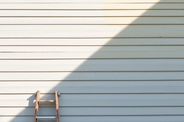 Horizontal wood siding in sunlight and shadow with a wooden ladder leaning against it