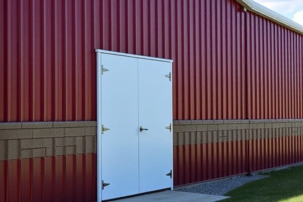 A steel building with red ribbed wall panels, white trim and a white double walk door