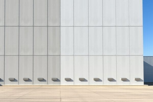A tall concrete tilt up warehouse wall with vertical panel joints under a clear blue sky